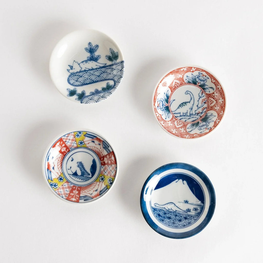 Set of four Japanese porcelain plates in gift box each with blue and red dinosaur design decoration.