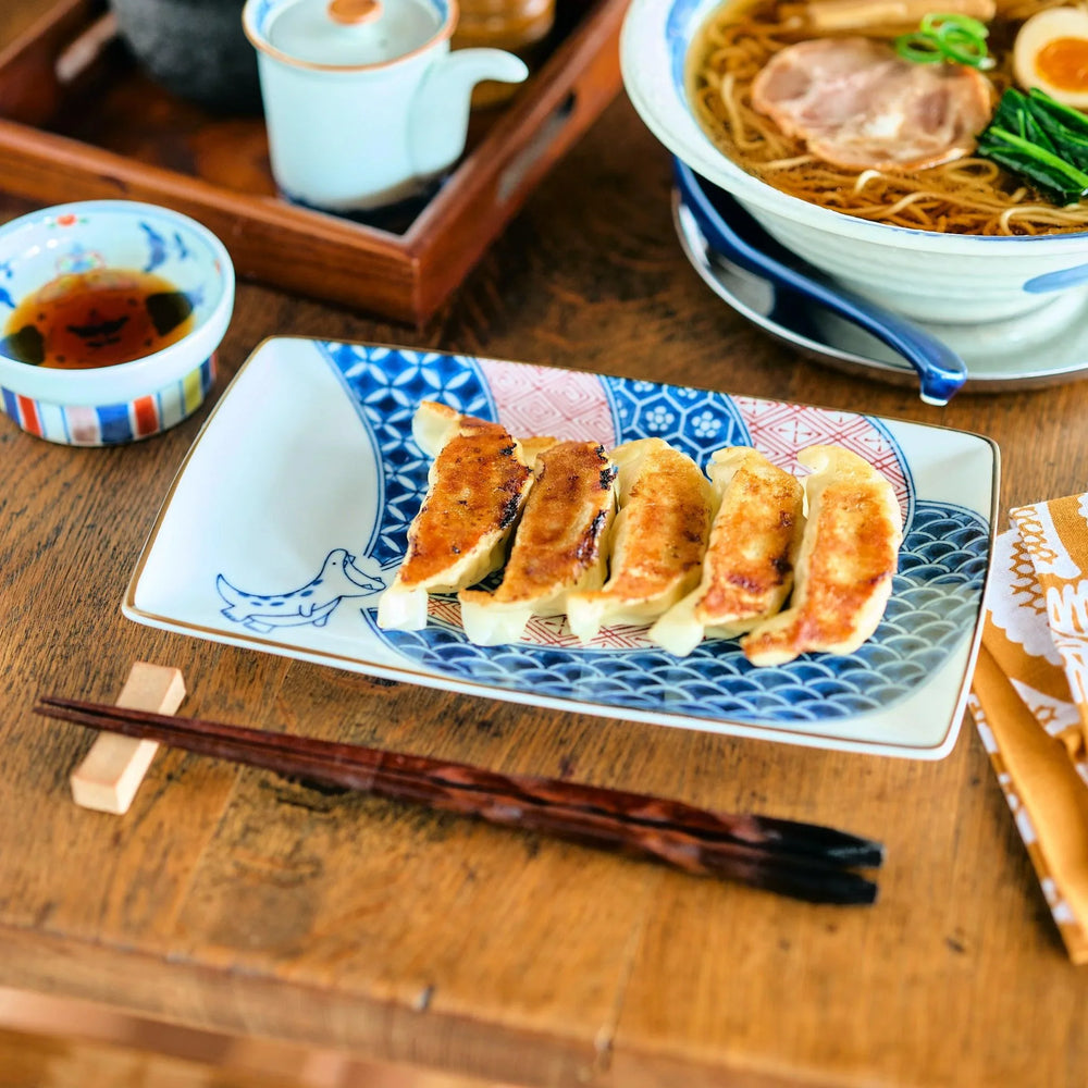 Rectangular plate with Edo patterns and blue dinosaur illustration served with golden pan fried gyoza.