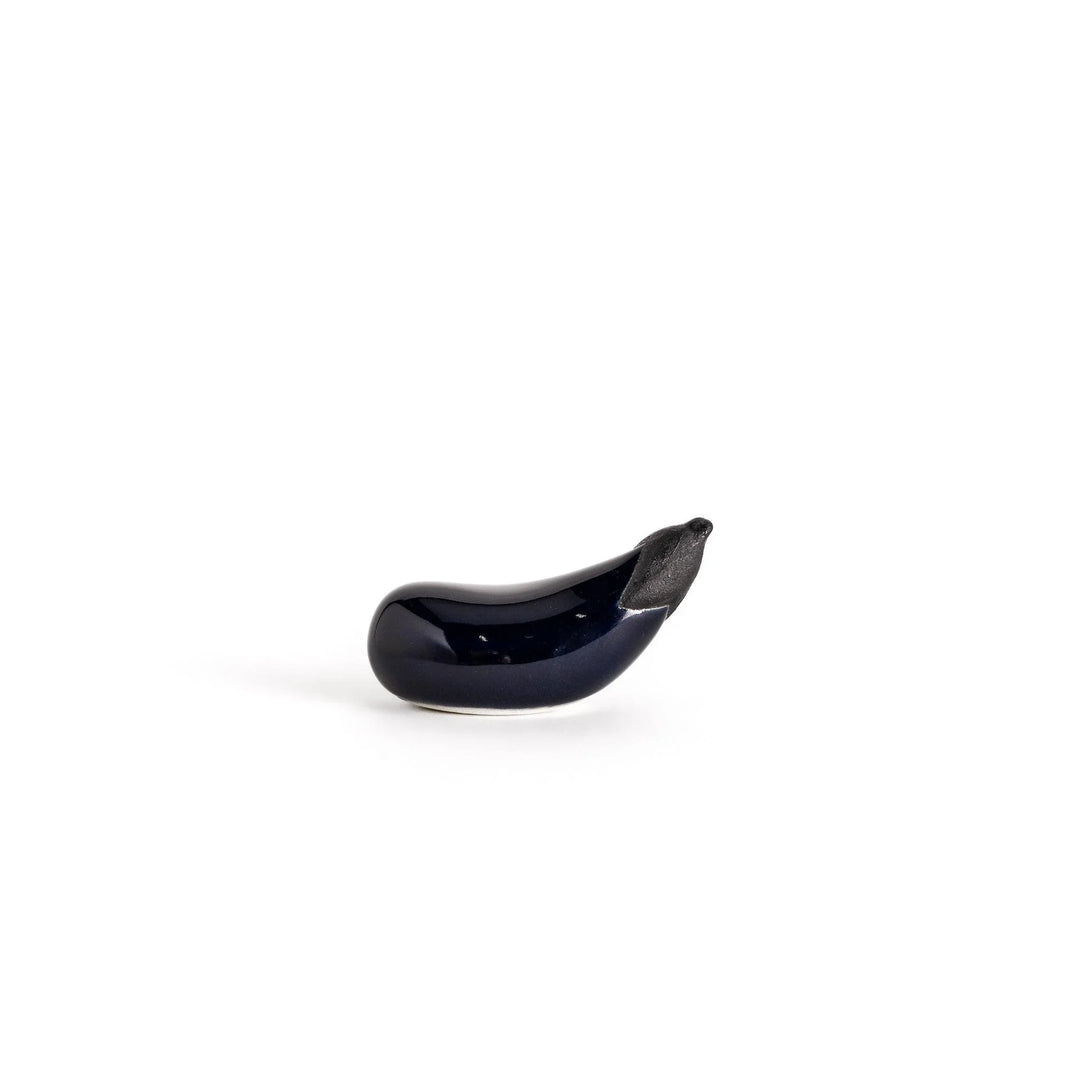 Glossy purple ceramic eggplant chopstick rest with black stem adding unique charm to Japanese table setting.