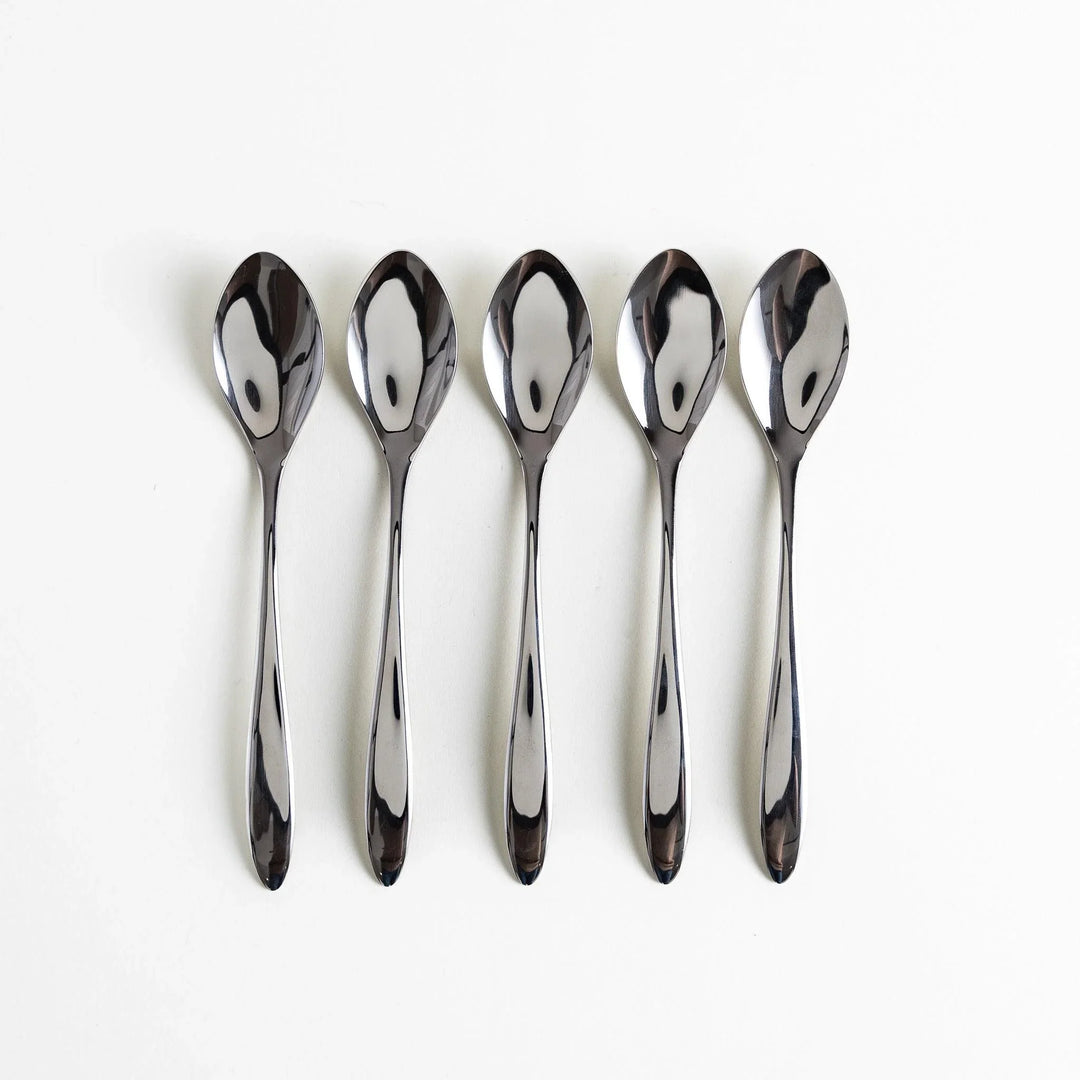 Five elegant stainless steel spoons arranged neatly in a row with polished surfaces reflecting light.