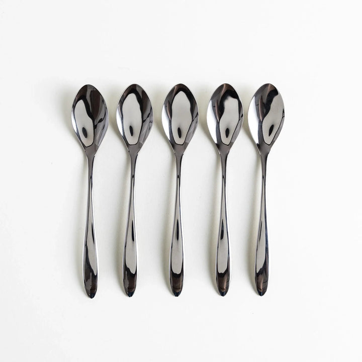 Five elegant stainless steel spoons arranged neatly in a row with polished surfaces reflecting light.
