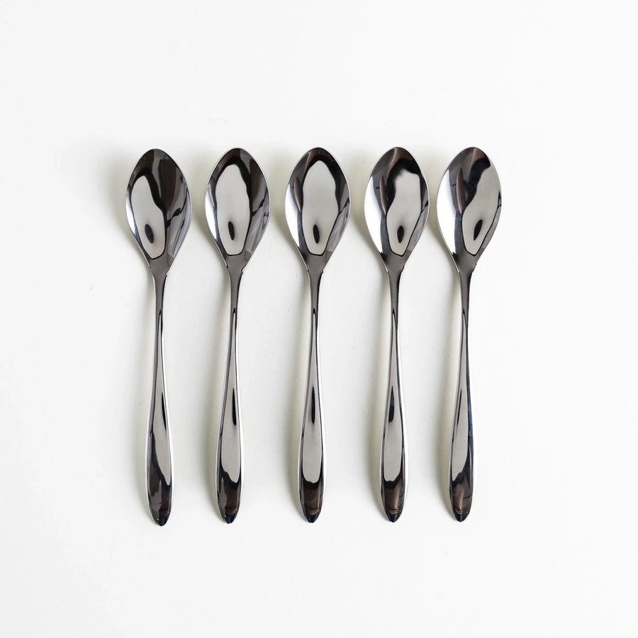 Five elegant stainless steel spoons arranged neatly in a row with polished surfaces reflecting light.