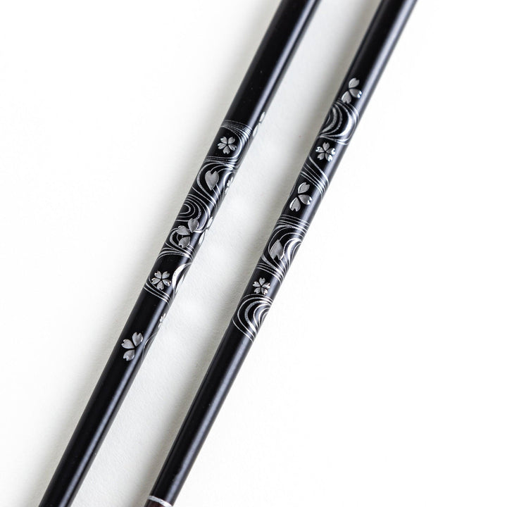 Two pairs of chopsticks, one black and one red, each adorned with intricate floral patterns on a dark background.