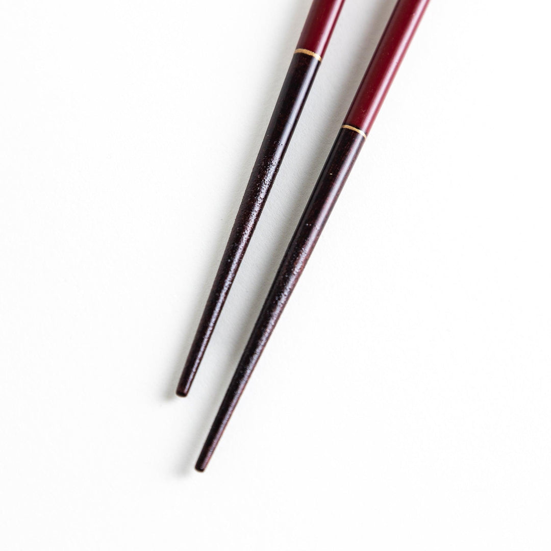 Two pairs of chopsticks, one black and one red, each adorned with intricate floral patterns on a dark background.