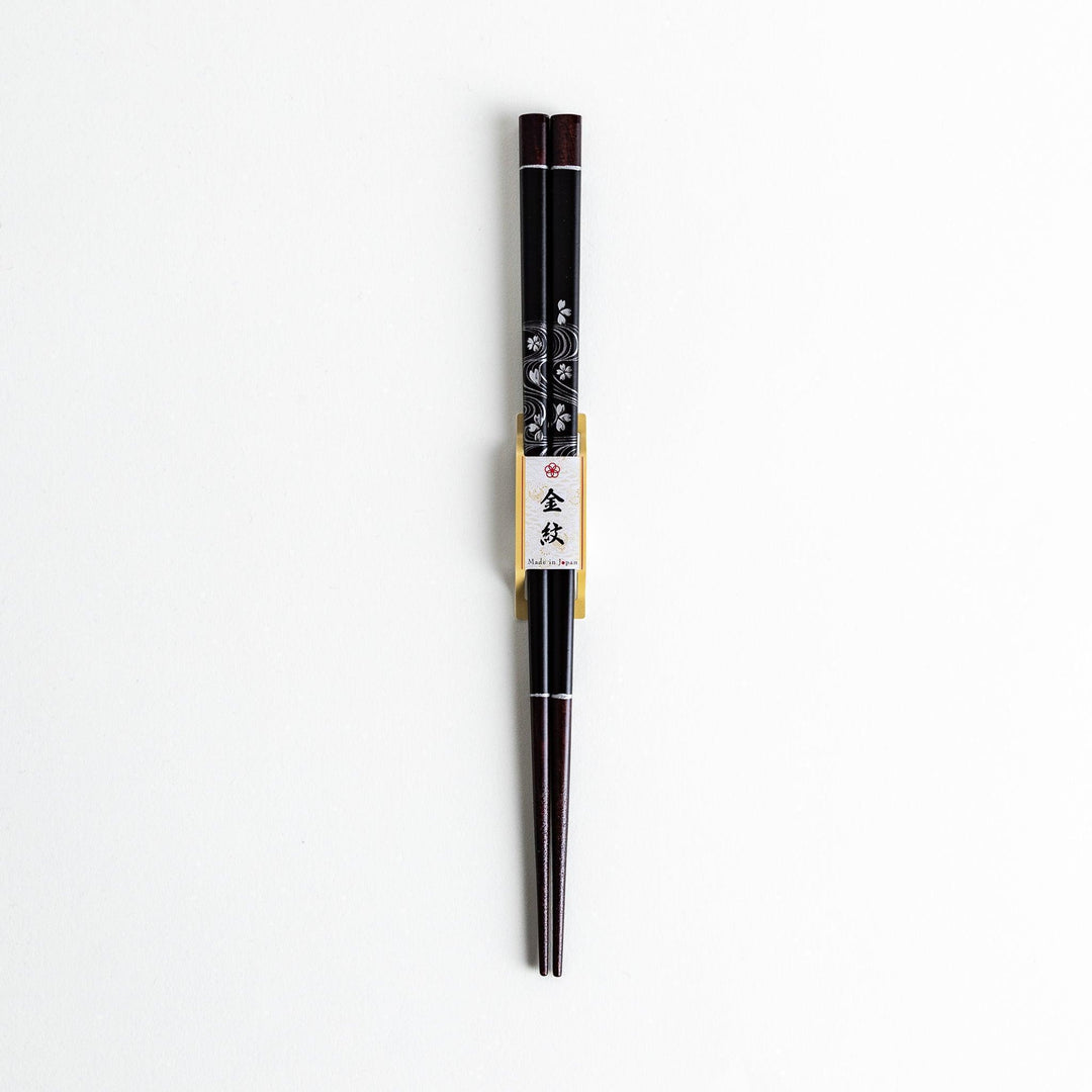 Two pairs of chopsticks, one black and one red, each adorned with intricate floral patterns on a dark background.