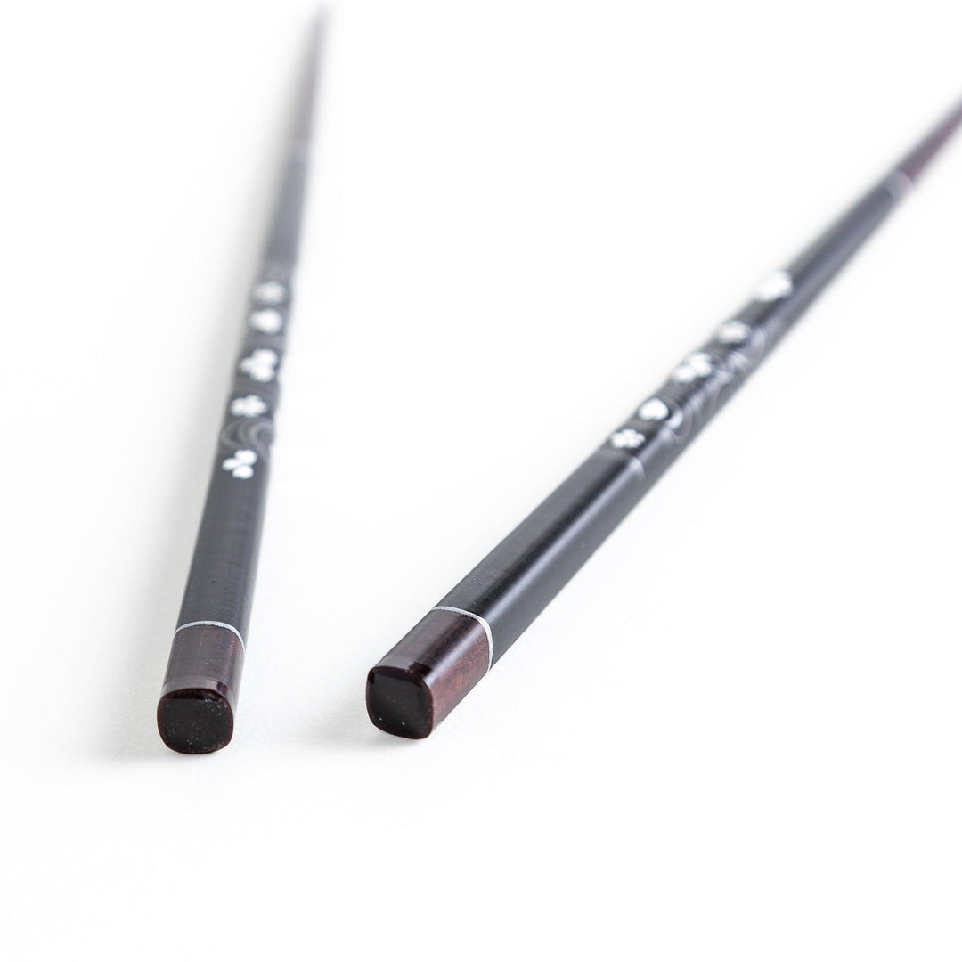 Two pairs of chopsticks, one black and one red, each adorned with intricate floral patterns on a dark background.