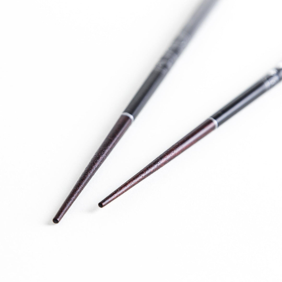 Two pairs of chopsticks, one black and one red, each adorned with intricate floral patterns on a dark background.