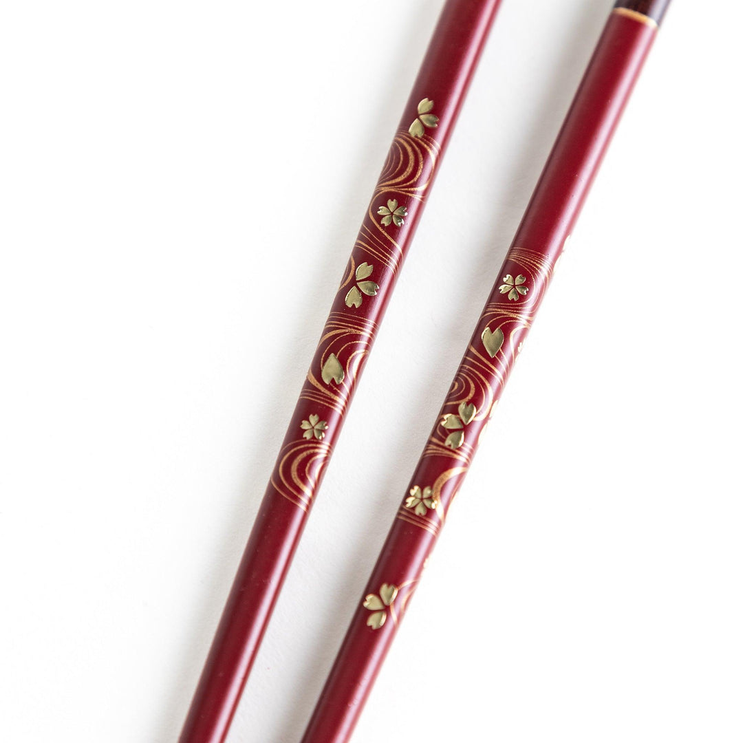 Two pairs of chopsticks, one black and one red, each adorned with intricate floral patterns on a dark background.