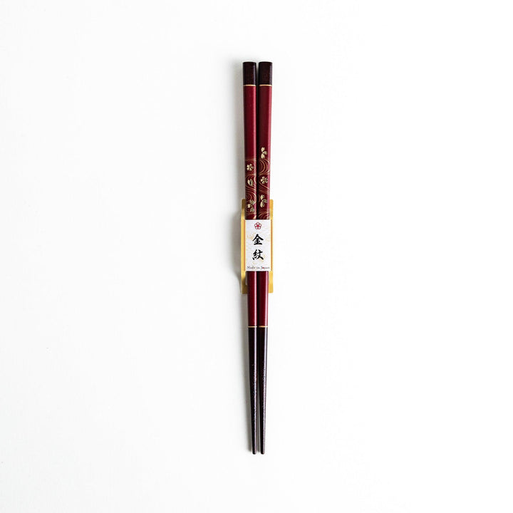 Two pairs of chopsticks, one black and one red, each adorned with intricate floral patterns on a dark background.