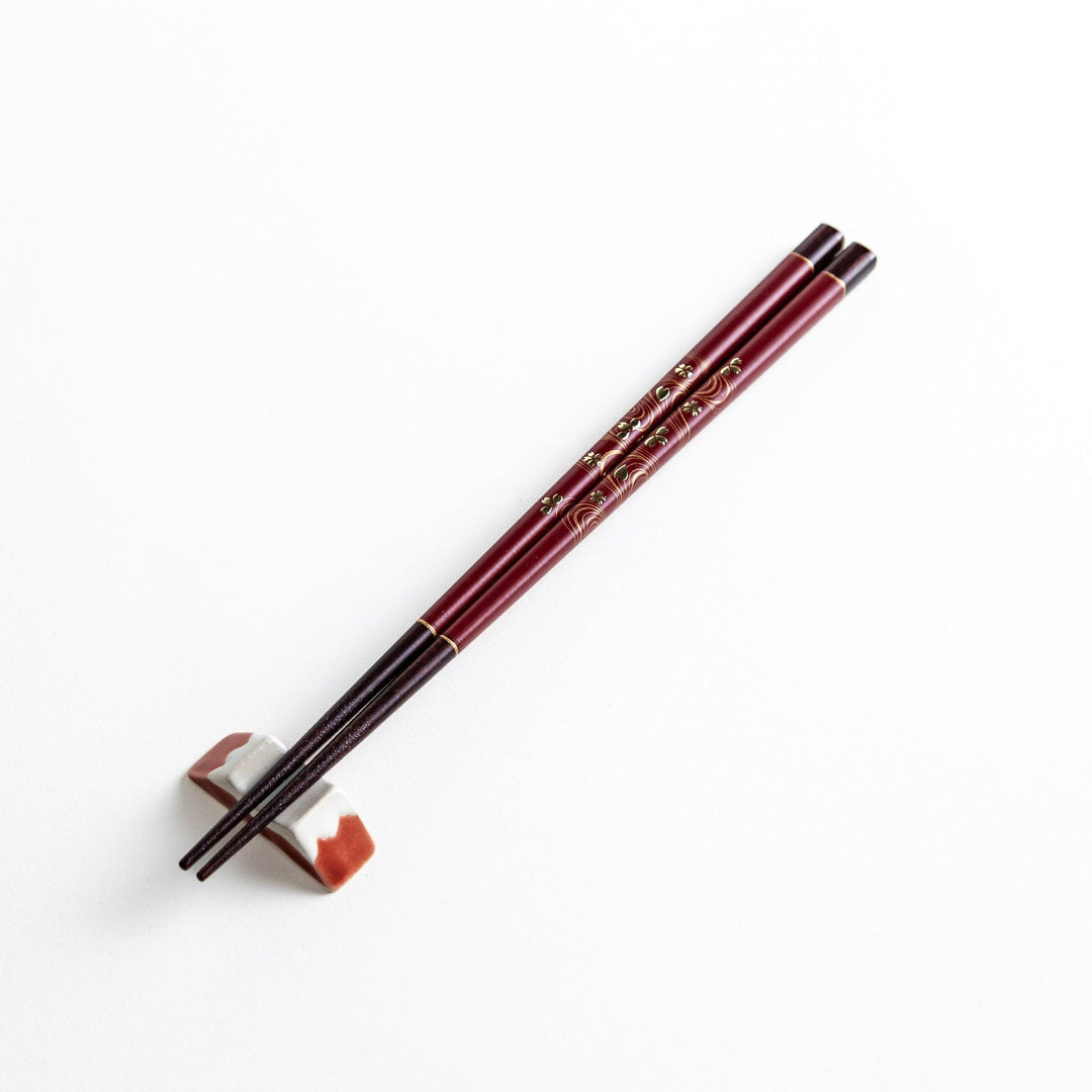Two pairs of chopsticks, one black and one red, each adorned with intricate floral patterns on a dark background.