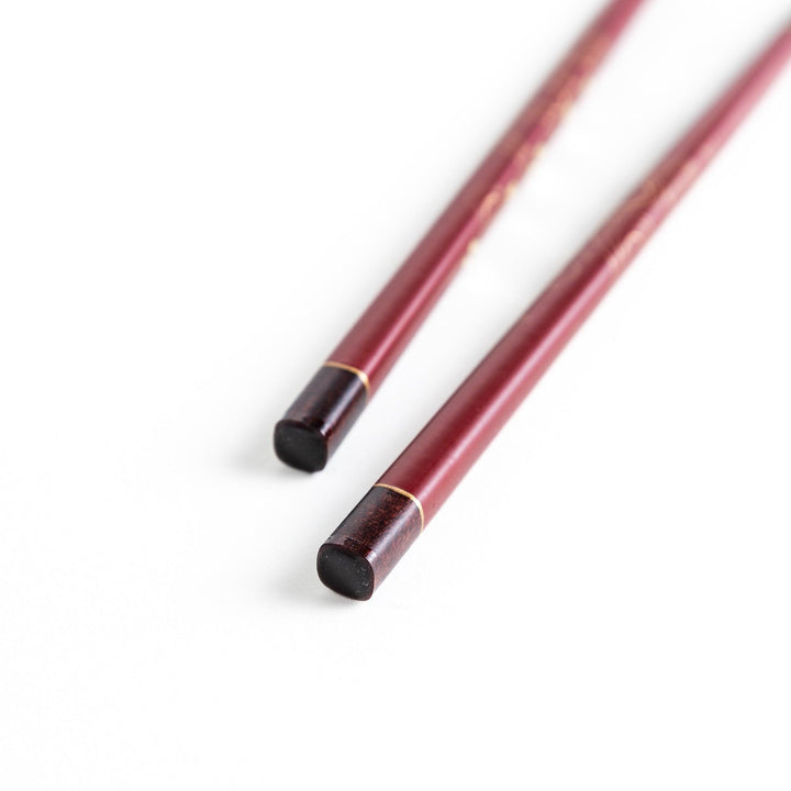 Two pairs of chopsticks, one black and one red, each adorned with intricate floral patterns on a dark background.