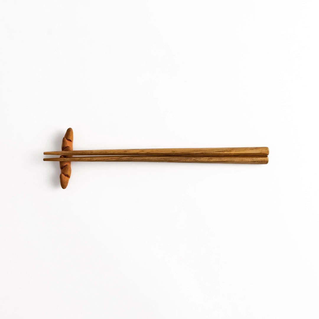 Epi Bread Chopstick Rest holding wooden chopsticks, showcasing its unique baguette design and practical functionality.