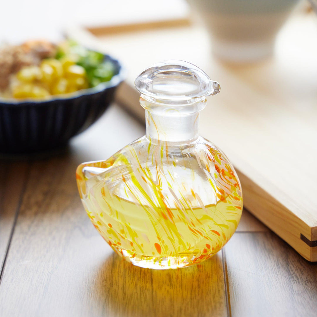 Ethereal Songbird Soy Sauce Dispenser made of handblown glass with yellow and orange swirls, placed on a wooden table.