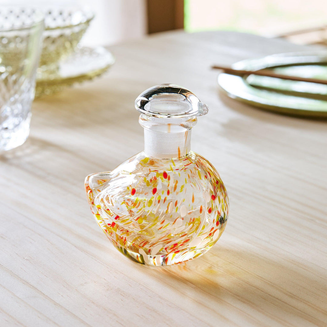 A handcrafted glass soy sauce dispenser shaped like a songbird, featuring warm amber and green patterns.