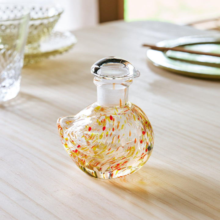 A handcrafted glass soy sauce dispenser shaped like a songbird, featuring warm amber and green patterns.