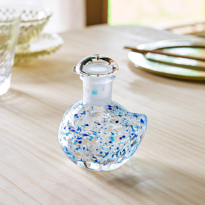 A clear glass soy sauce dispenser in a bird shape, decorated with scattered blue and white speckles.