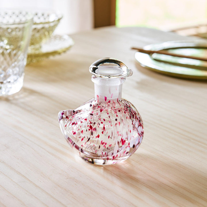 A glass soy sauce dispenser shaped like a bird, adorned with delicate pink and red speckles and a clear glass stopper.