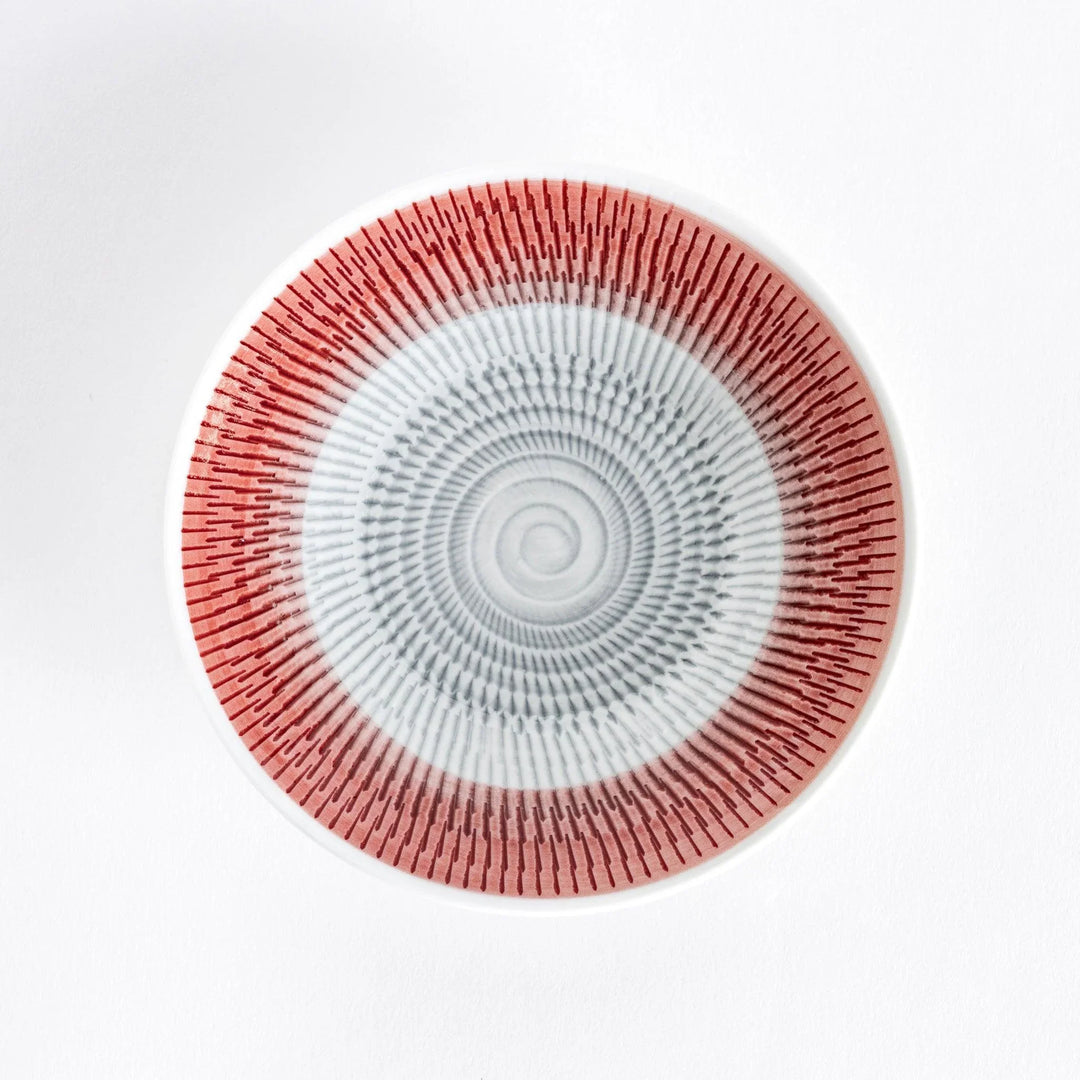 A red dessert plate with bold radiating spiral-striped patterns, captured from the front.