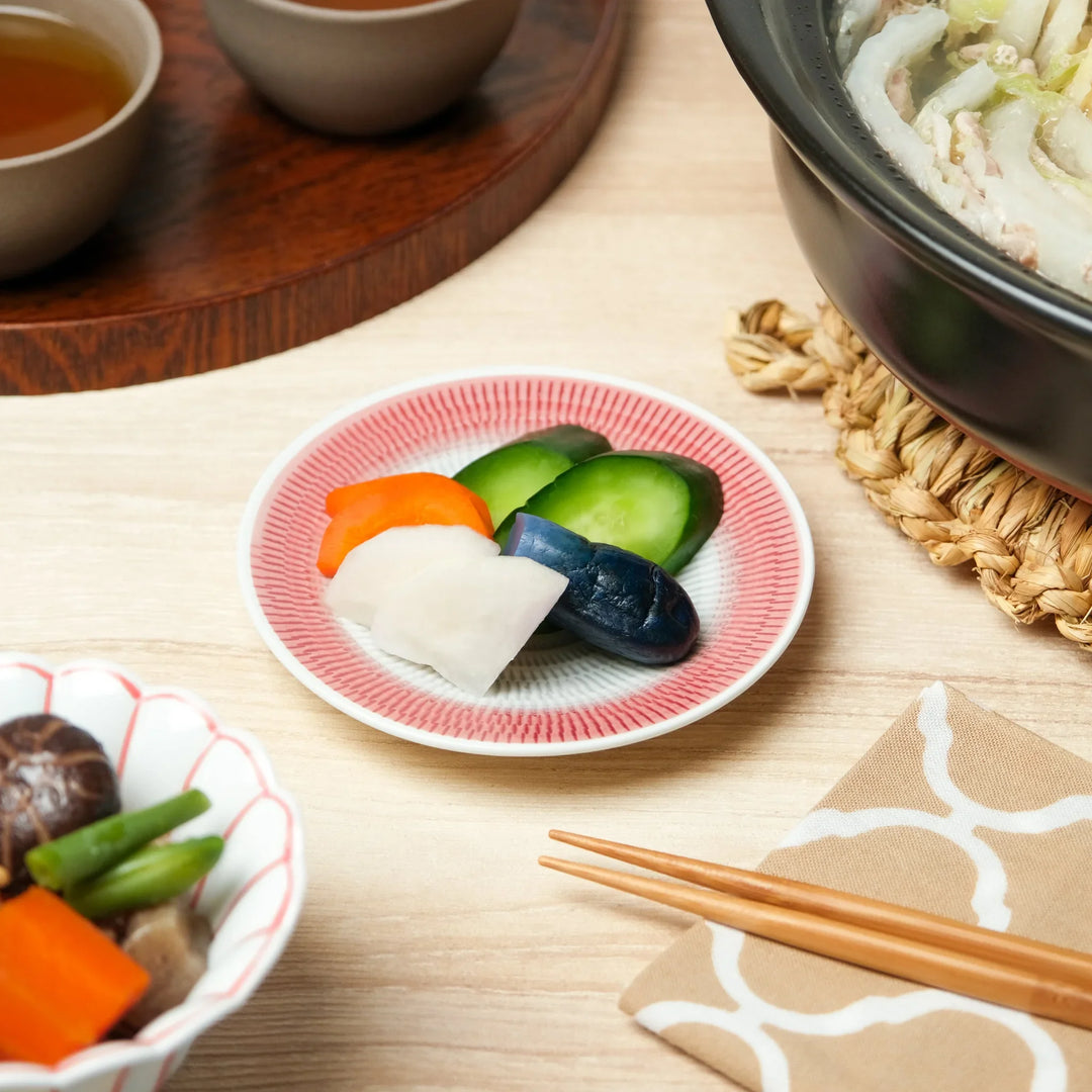 Japanese side dish plate with red geometric pattern holding assorted pickled vegetables for traditional meal.