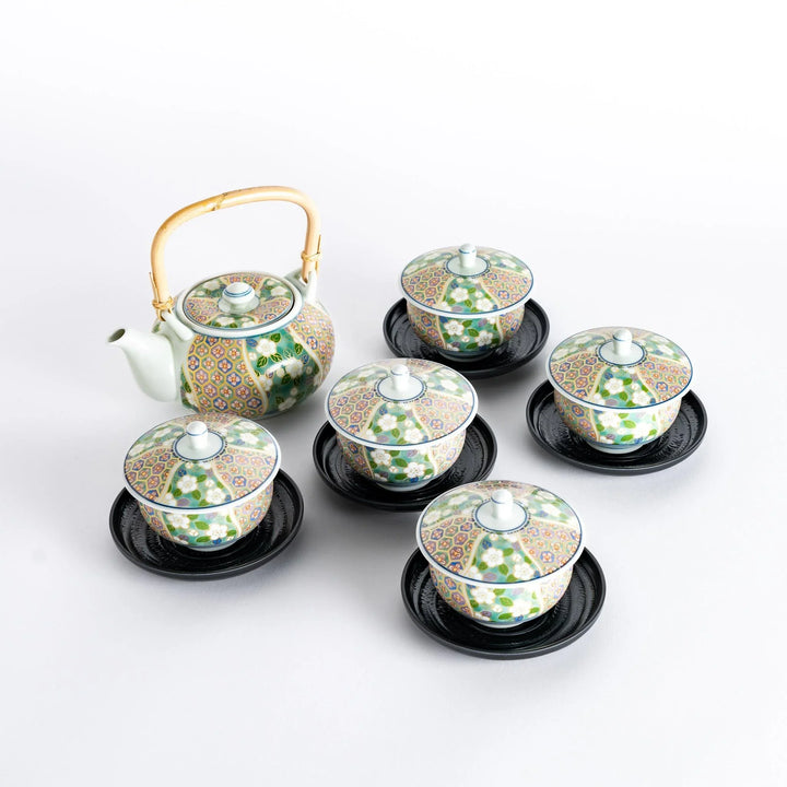 Japanese tea set with bamboo handled teapot and five floral cups with lids on black saucers.