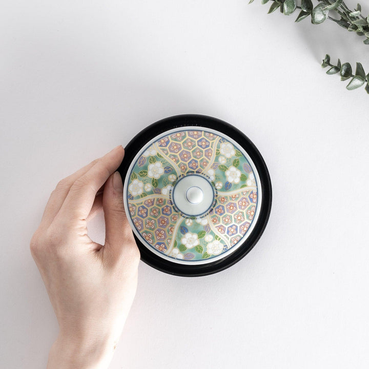 Top view of tea cup with hand placed on the side, featuring a floral pattern with green and pink tones.