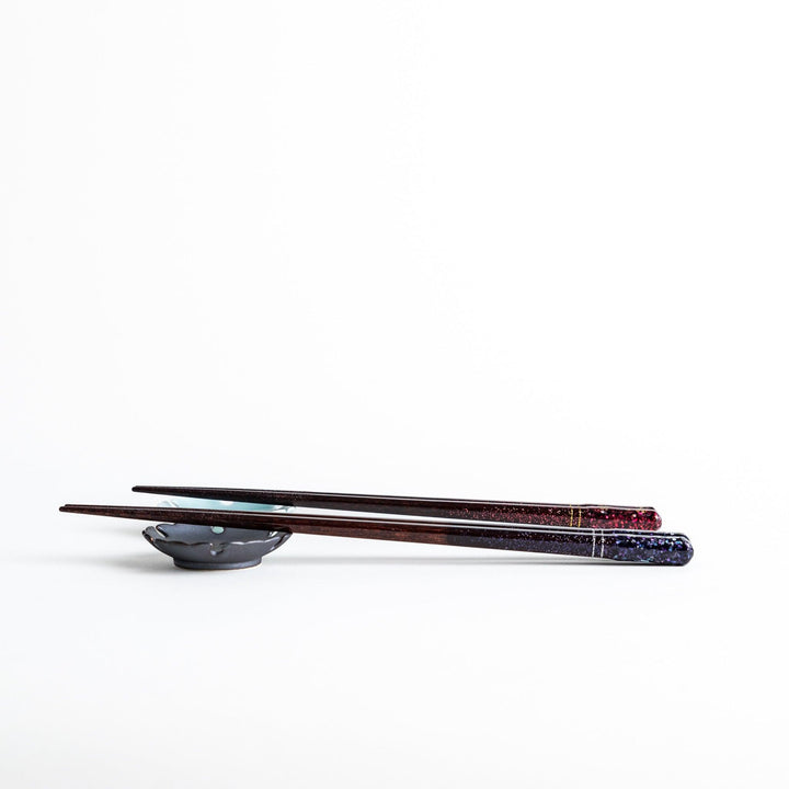 A pair of chopsticks with a sleek design featuring glitter accents and small floral patterns in deep red and navy blue, adding a touch of sparkle to your dining experience.