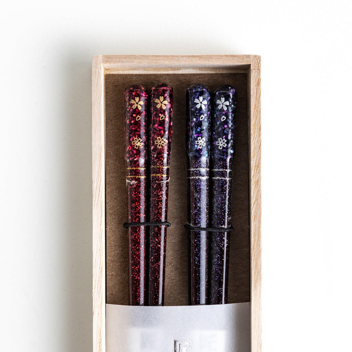 A pair of chopsticks with a sleek design featuring glitter accents and small floral patterns in deep red and navy blue, adding a touch of sparkle to your dining experience.