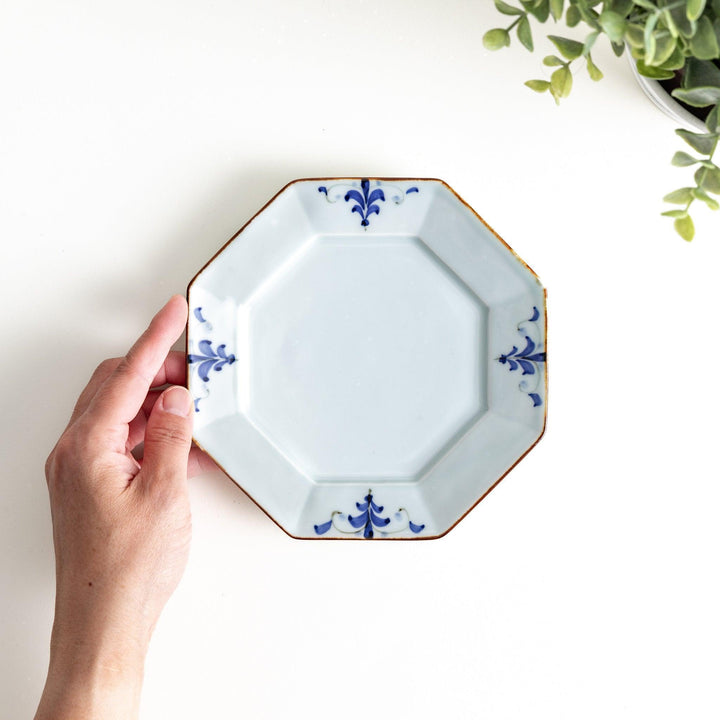 Octagonal white porcelain dessert plate with a blue floral motif and brown accent trim.