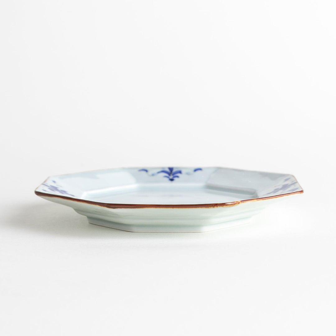 Octagonal white porcelain dessert plate with a blue floral motif and brown accent trim.