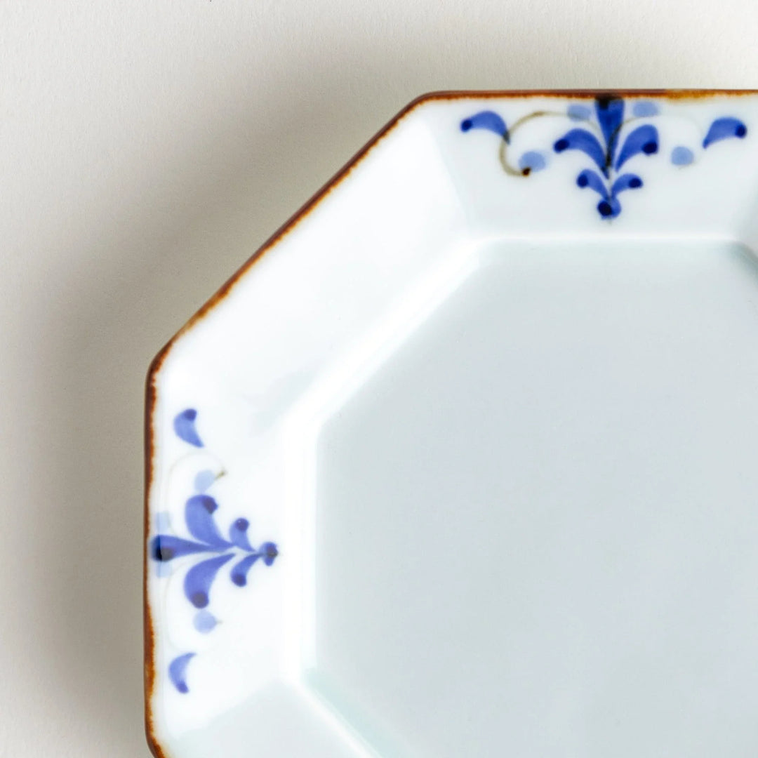 Octagonal white porcelain dessert plate with a blue floral motif and brown accent trim.