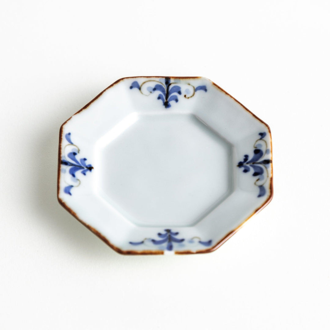 Octagonal white porcelain small sauce dish with a blue floral motif and brown accent trim.