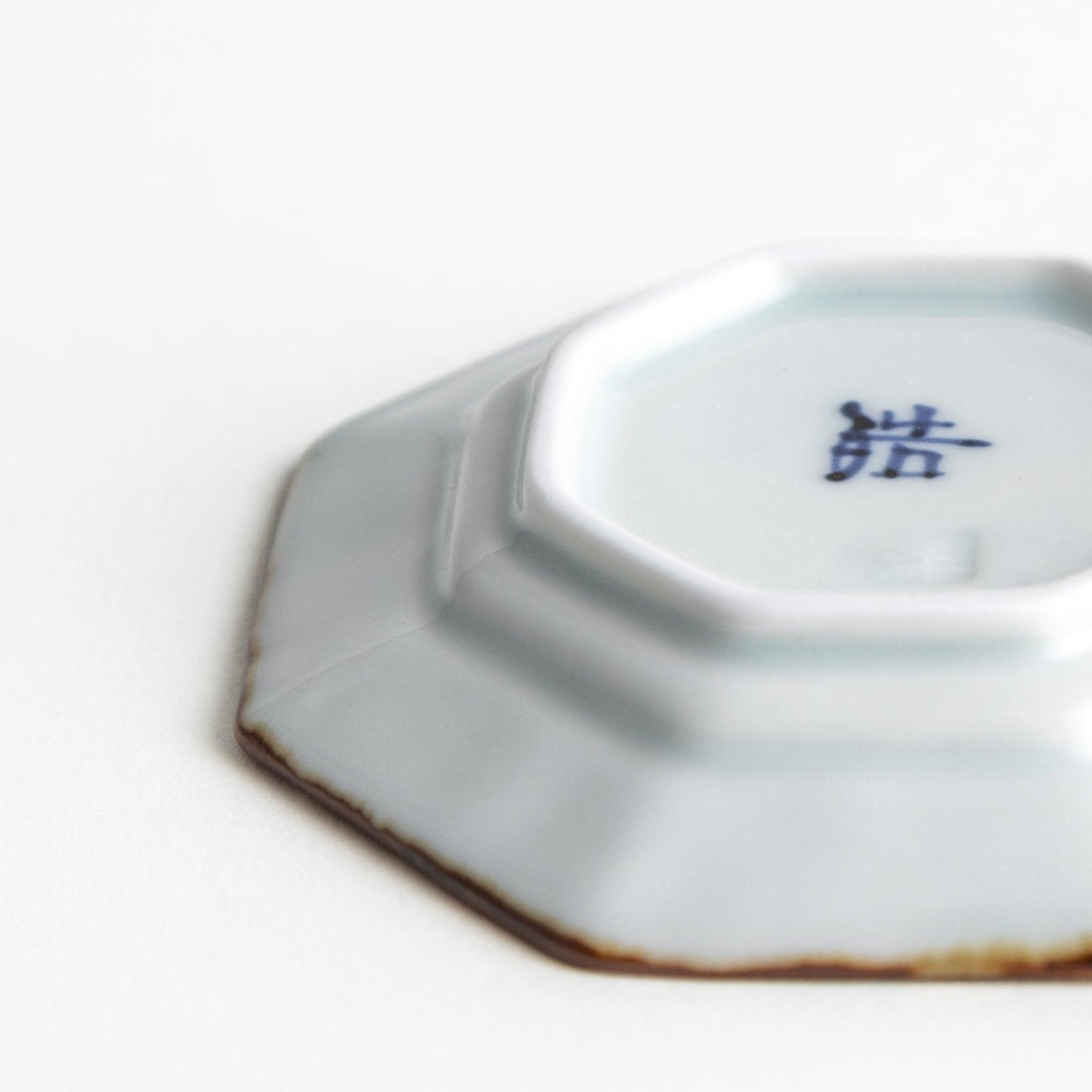 Octagonal white porcelain small sauce dish with a blue floral motif and brown accent trim.