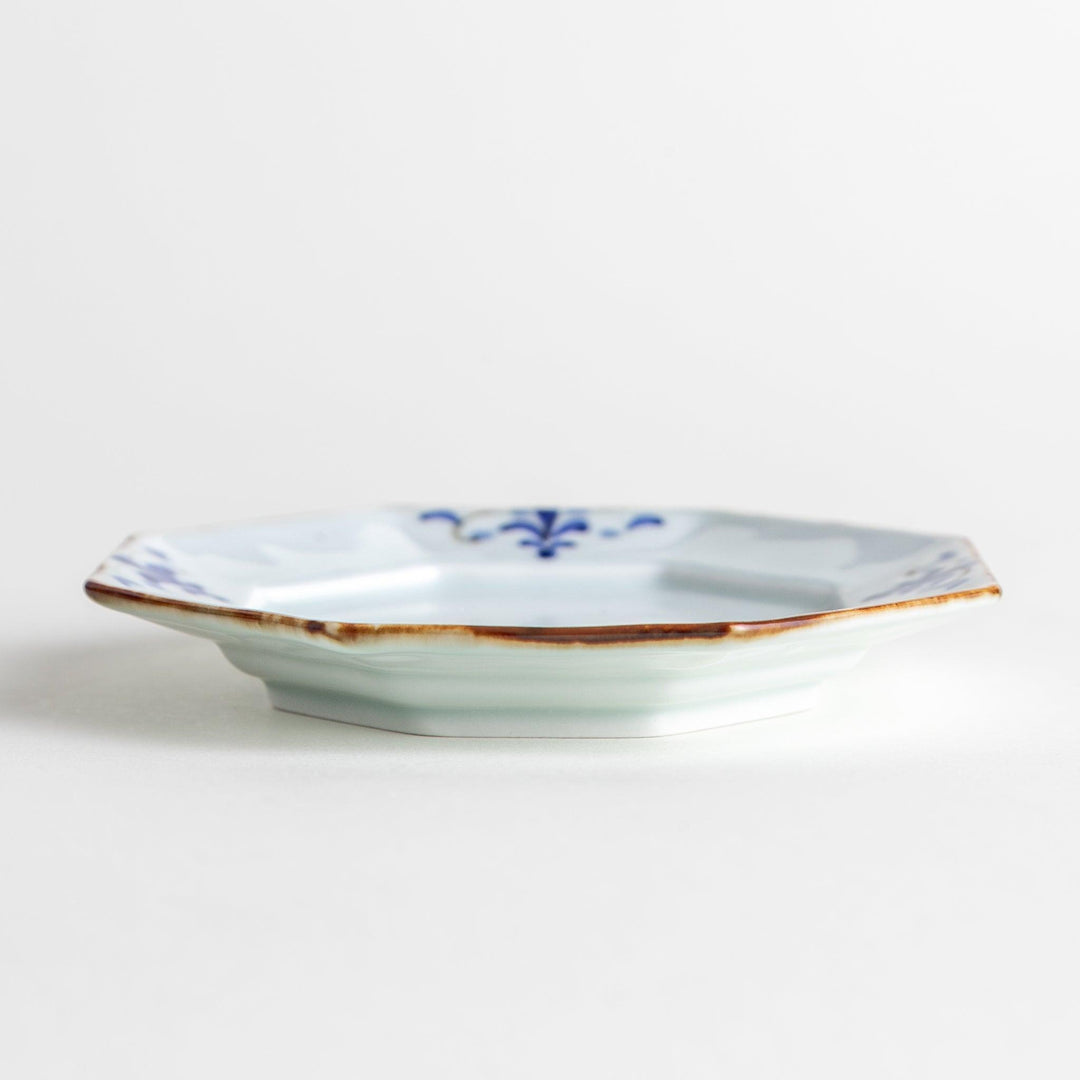 Octagonal white porcelain sauce dish with a blue floral motif and brown accent trim.