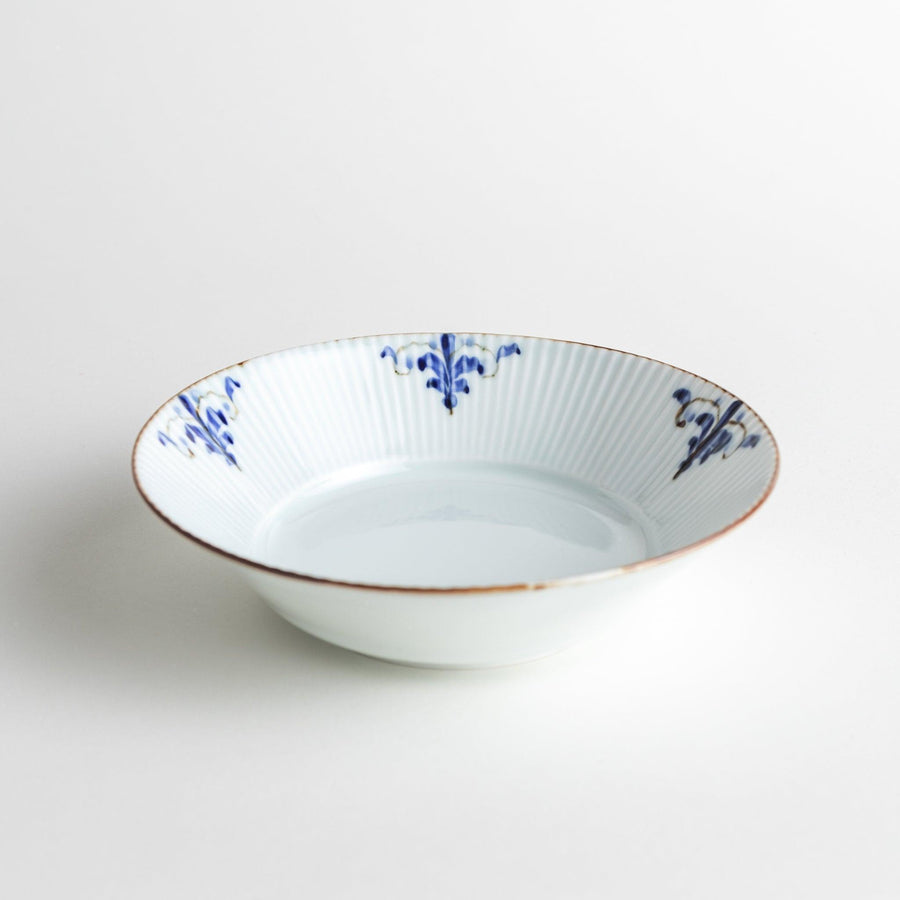 A round, shallow white bowl with blue floral patterns and a ribbed design along the edges and brown accent trim.