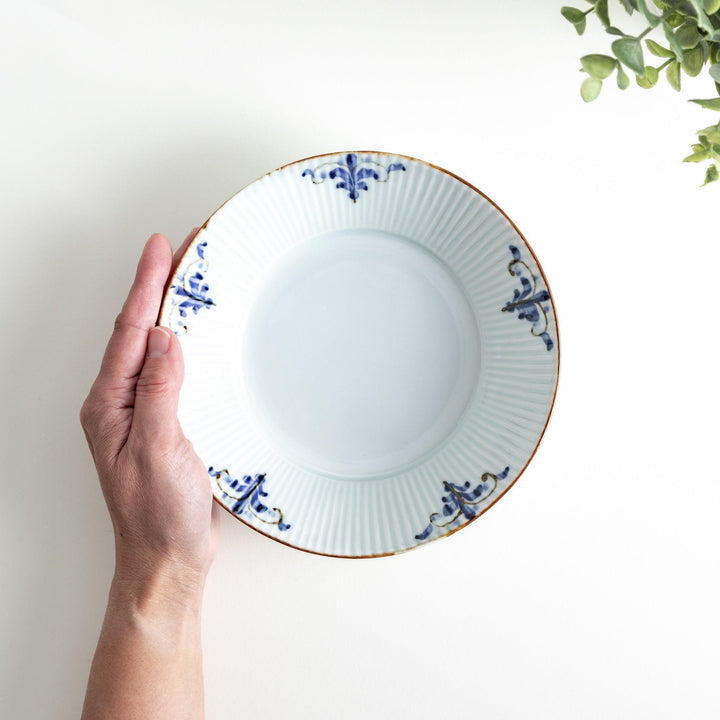 A round, shallow white bowl with blue floral patterns and a ribbed design along the edges and brown accent trim.