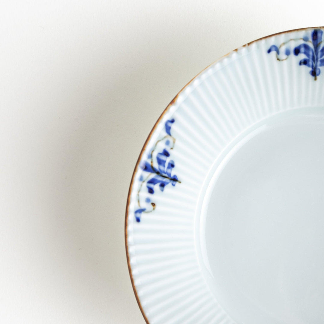 A round, shallow white bowl with blue floral patterns and a ribbed design along the edges and brown accent trim.