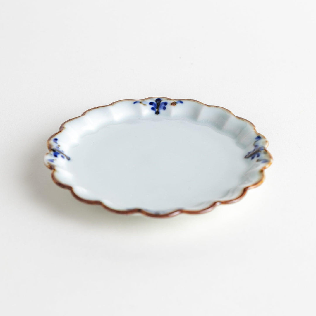 Round white porcelain sauce dish with scalloped edges, adorned with a simple blue floral pattern and brown accent trim.