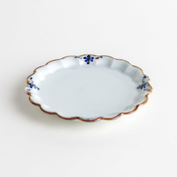 Round white porcelain sauce dish with scalloped edges, adorned with a simple blue floral pattern and brown accent trim.