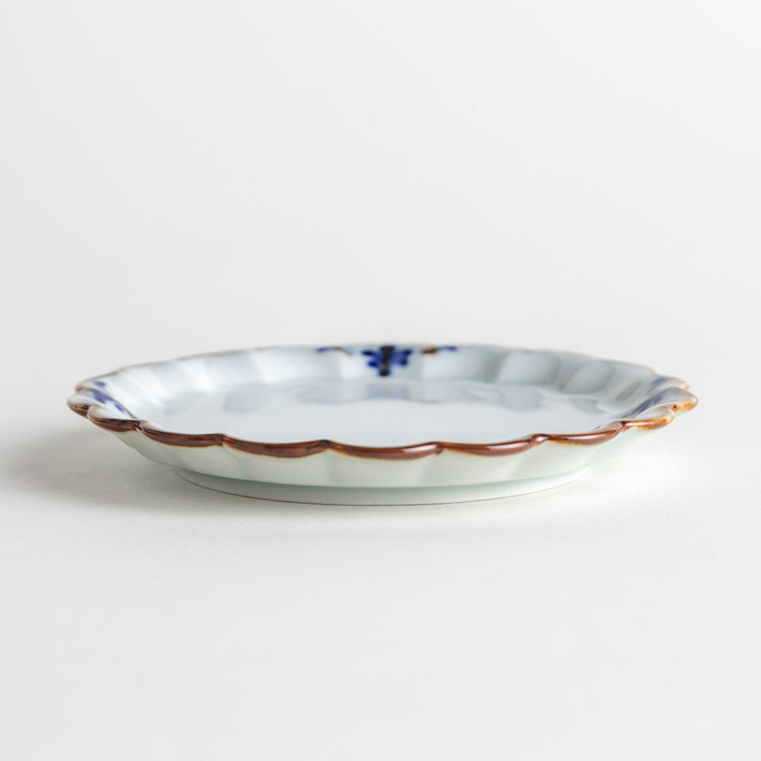 Round white porcelain sauce dish with scalloped edges, adorned with a simple blue floral pattern and brown accent trim.