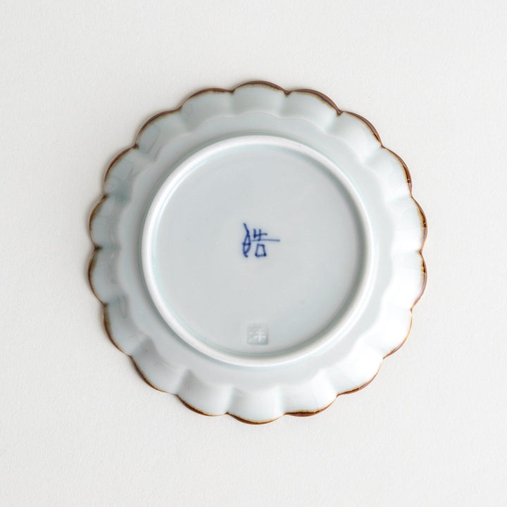 Round white porcelain sauce dish with scalloped edges, adorned with a simple blue floral pattern and brown accent trim.