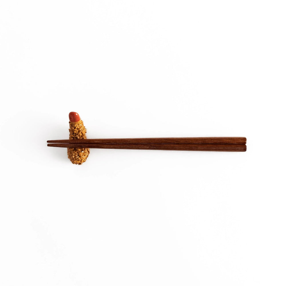Fried shrimp chopstick rest with golden crunchy texture and red tip adding playful detail to dining.