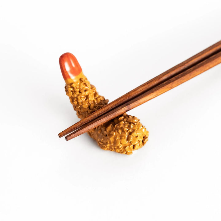Fried shrimp chopstick rest with golden crunchy texture and red tip adding playful detail to dining.