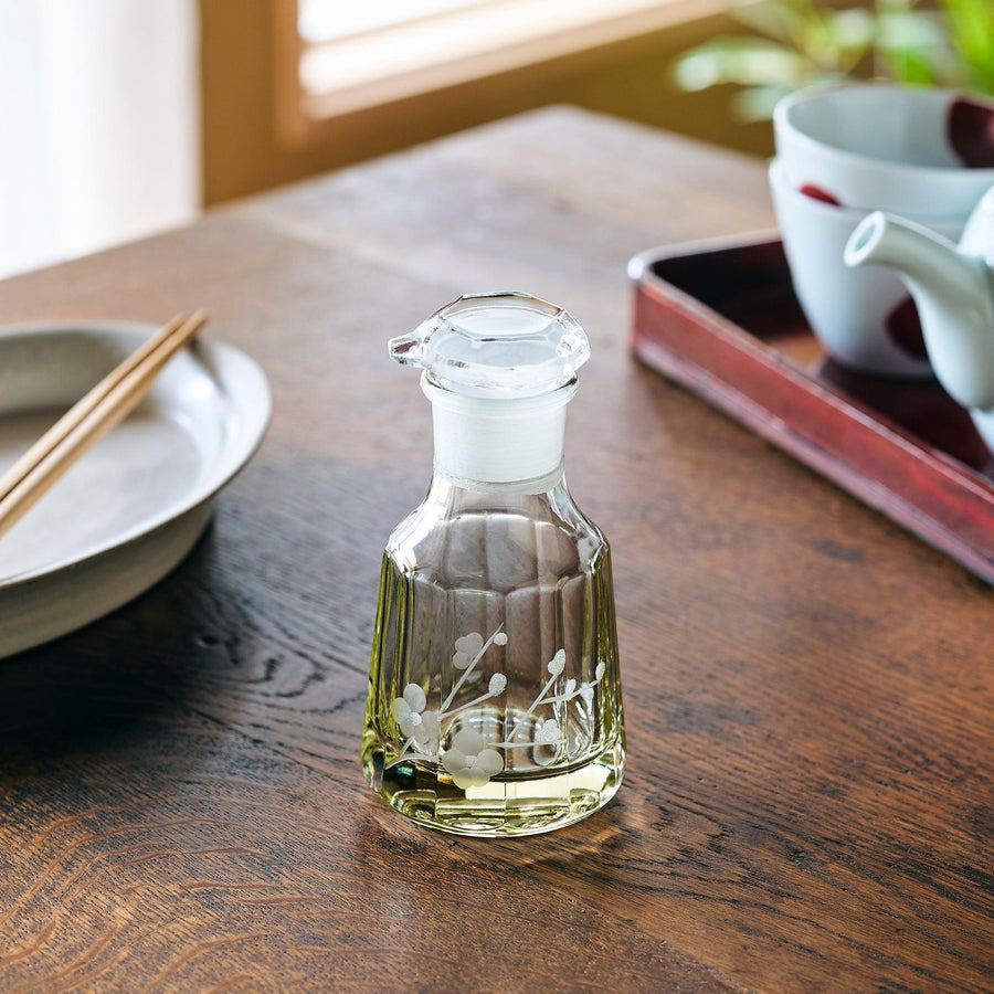 Elegant glass dispenser featuring a delicate floral motif, filled with light-colored liquid on a wooden dining table.