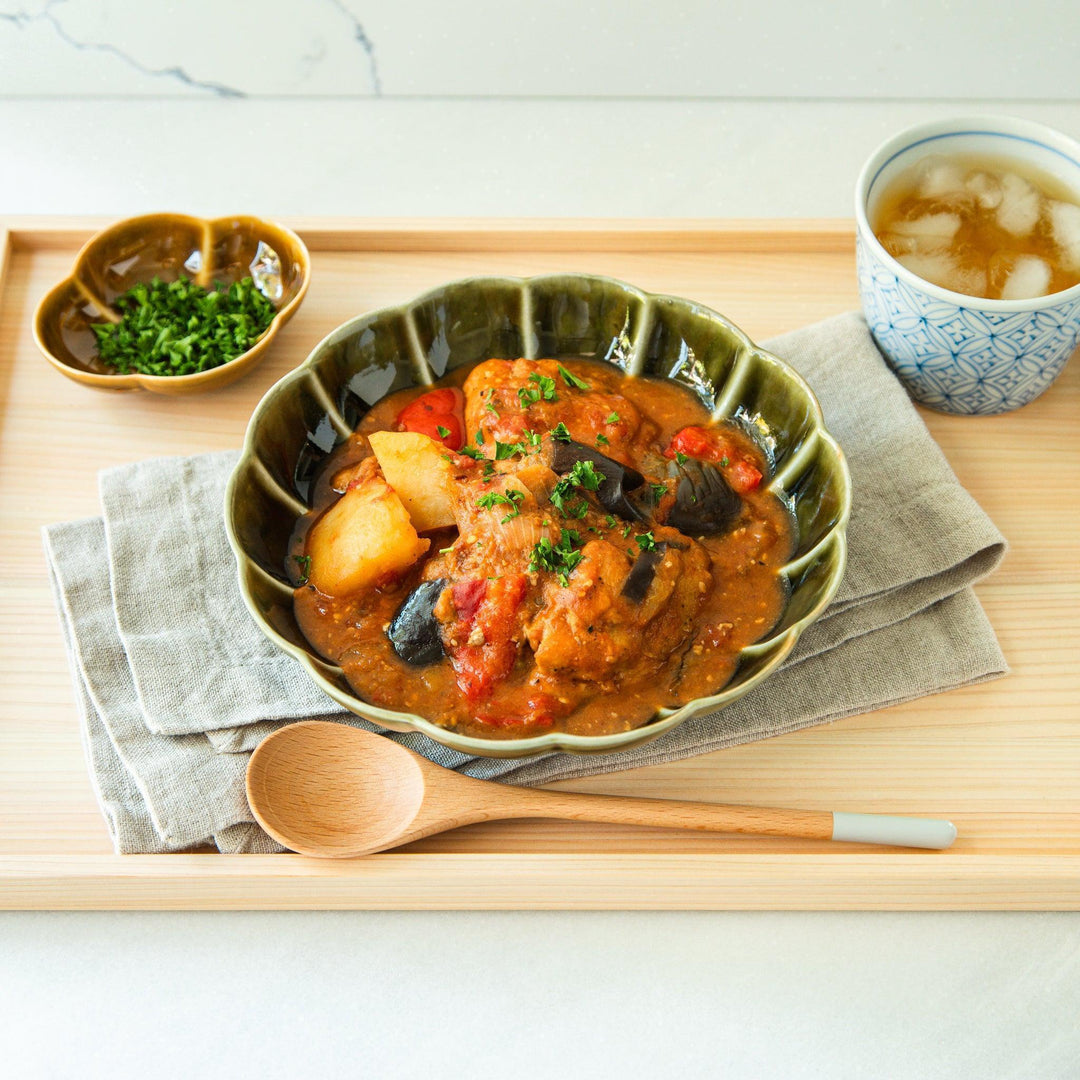 Blue patterned Japanese tea bowl with iced tea on tray beside green pasta bowl of miso tomato chicken stew.