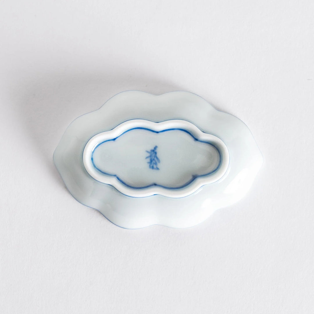 Bottom view of a decorative sauce dish featuring a small maker's mark on its smooth white surface.