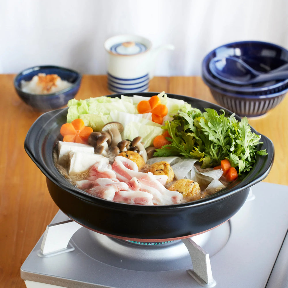 Japanese donabe clay pot filled with pork, tofu, mushrooms, and vegetables simmering on tabletop stove, perfect for hot pot.