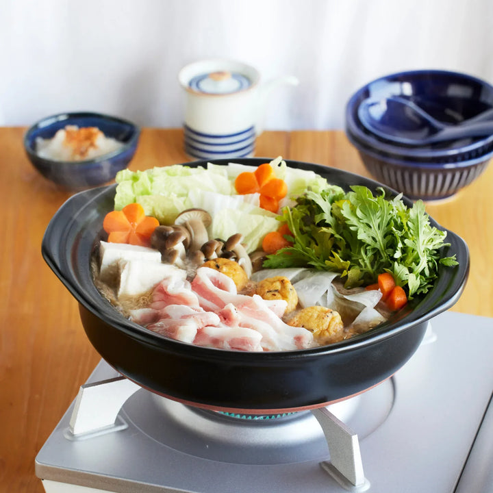 Japanese donabe clay pot filled with pork, tofu, mushrooms, and vegetables simmering on tabletop stove, perfect for hot pot.