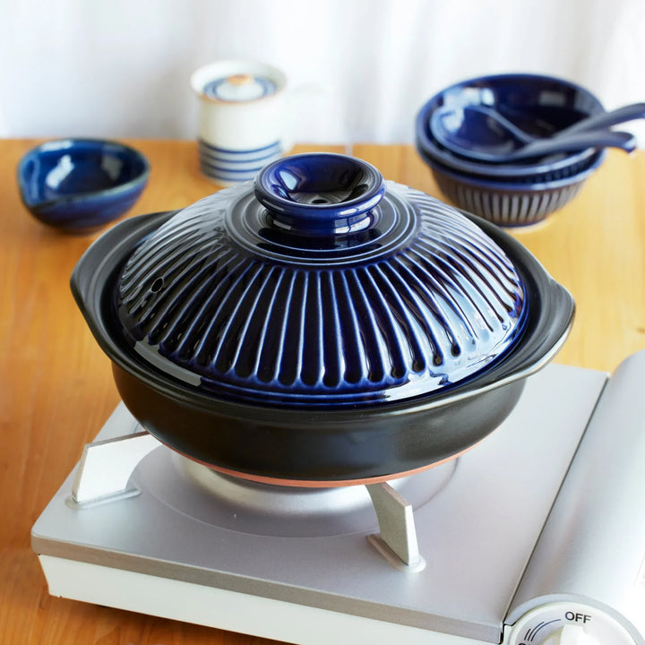 Indigo Donabe Japanese clay pot with ridged lid on tabletop gas stove, traditional ceramic cookware for hot pot and stews.