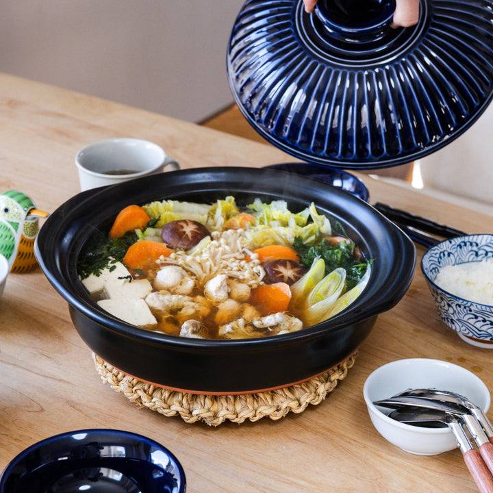 Japanese donabe hot pot with vegetables tofu mushrooms and chicken served at the table with rice bowls