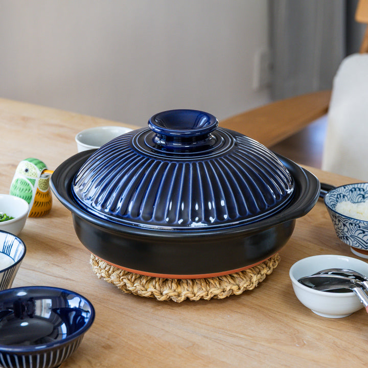 Blue ceramic Kikka family size donabe on a wooden table with various bowls and items around